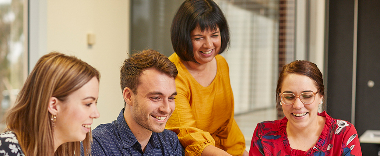 Students and trainer looking at computer smiling